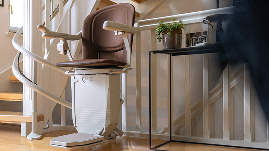 Auf einer geschwungenen Treppe in einem Haus ist ein Treppenlift mit braunem Sitz installiert.