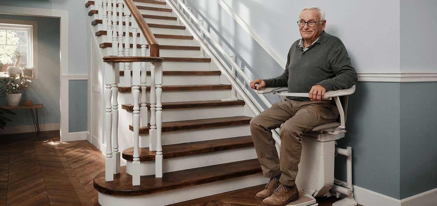 Ein Senior sitzt auf einem gemieteten Treppenlift am unteren Ende einer Treppe